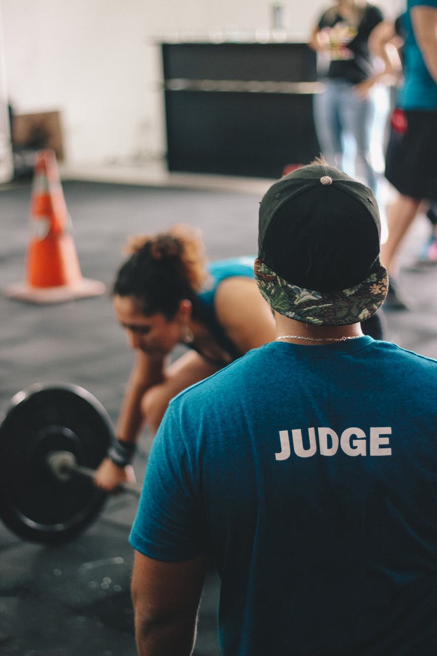 man in blue crew neck shirt staring at woman trying to lift barbell
